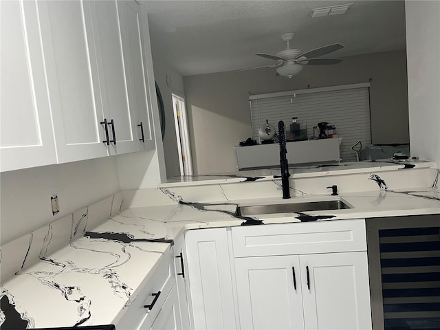 kitchen featuring sink, light stone countertops, beverage cooler, and white cabinets