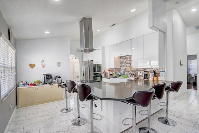 kitchen with stainless steel refrigerator with ice dispenser, a kitchen bar, kitchen peninsula, and island exhaust hood