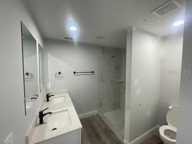 bathroom featuring tiled shower, vanity, toilet, and hardwood / wood-style floors