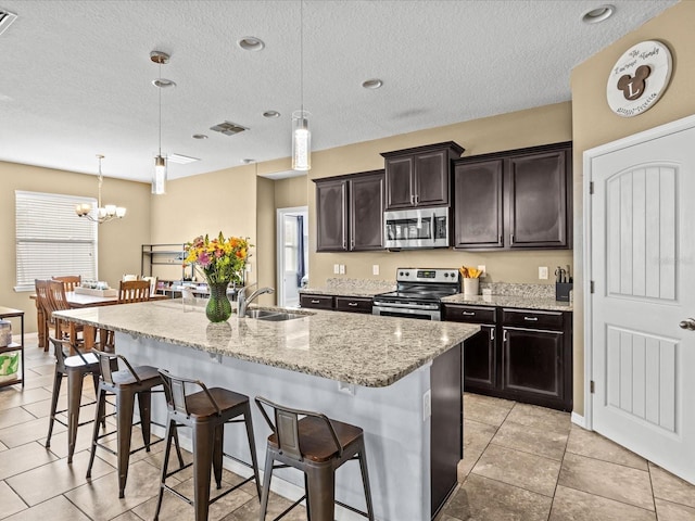 kitchen with a kitchen bar, decorative light fixtures, dark brown cabinets, appliances with stainless steel finishes, and a kitchen island with sink