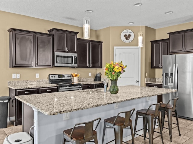 kitchen featuring pendant lighting, appliances with stainless steel finishes, a kitchen island with sink, and sink