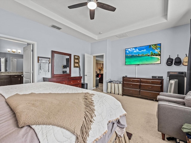 bedroom with light carpet, a tray ceiling, ceiling fan, and ensuite bathroom