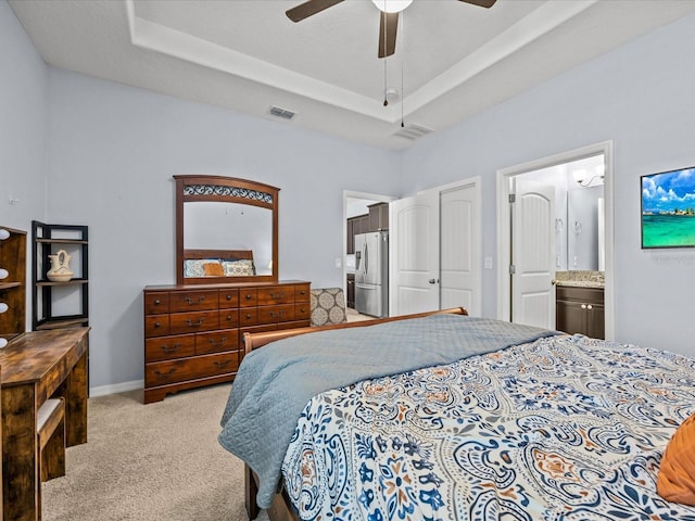 carpeted bedroom with a tray ceiling, stainless steel fridge, ensuite bath, and ceiling fan