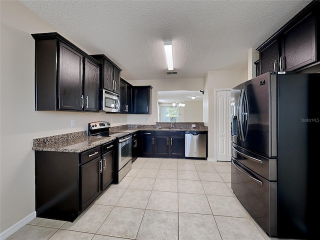 kitchen with light tile patterned flooring, appliances with stainless steel finishes, sink, and dark stone counters