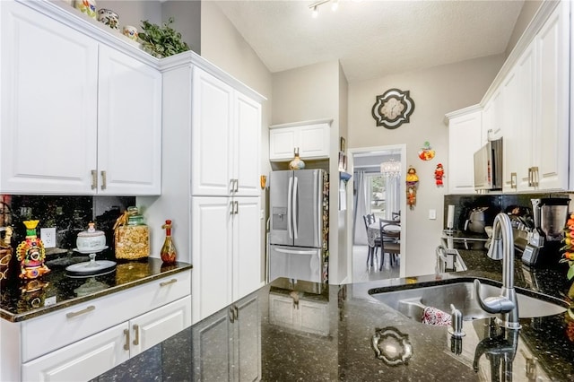 kitchen featuring white cabinets, sink, stainless steel fridge, and dark stone counters