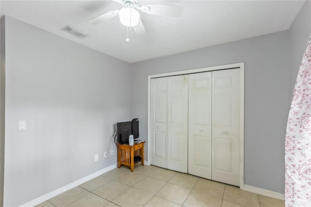 unfurnished bedroom featuring light tile patterned flooring, ceiling fan, a textured ceiling, and a closet