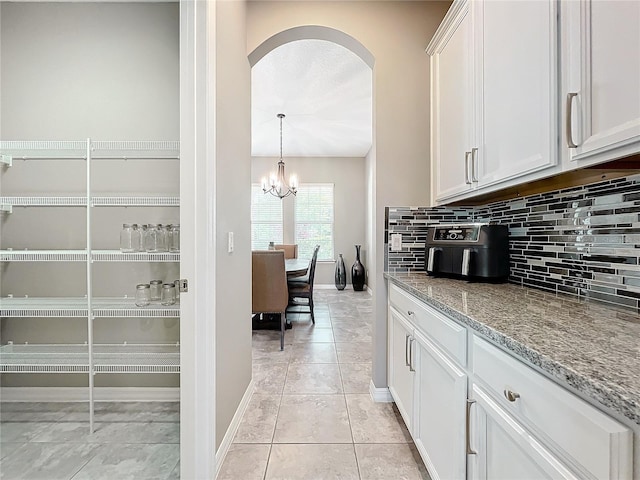 kitchen featuring pendant lighting, light tile patterned floors, white cabinetry, backsplash, and light stone countertops