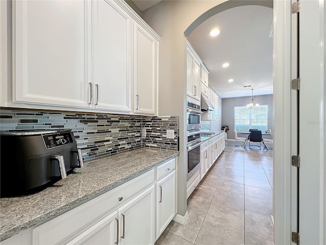 kitchen with light tile patterned floors, white cabinetry, an inviting chandelier, tasteful backsplash, and light stone countertops