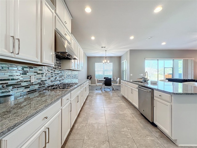 kitchen featuring white cabinetry, light stone counters, hanging light fixtures, appliances with stainless steel finishes, and an island with sink