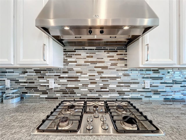 kitchen with stainless steel gas stovetop, light stone countertops, extractor fan, and white cabinets