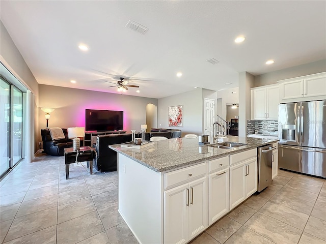 kitchen featuring appliances with stainless steel finishes, white cabinetry, sink, light stone counters, and a center island with sink