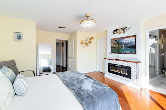 bedroom featuring a tile fireplace, wood-type flooring, and ensuite bathroom