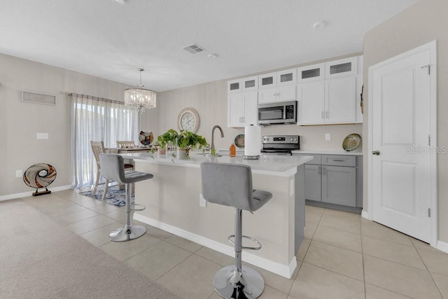 kitchen featuring a breakfast bar, white cabinetry, hanging light fixtures, a kitchen island with sink, and stainless steel appliances