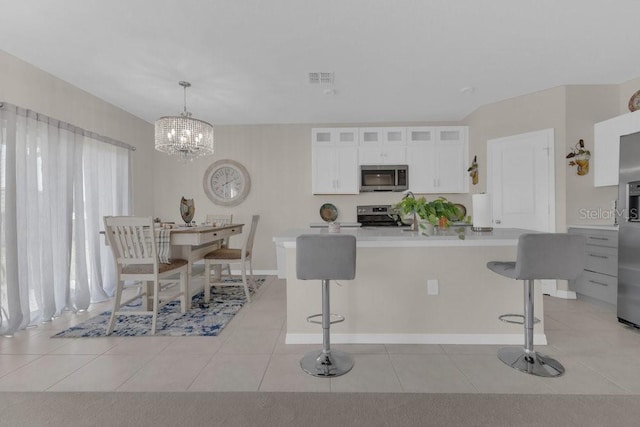 kitchen featuring a breakfast bar, decorative light fixtures, light tile patterned floors, stainless steel appliances, and white cabinets