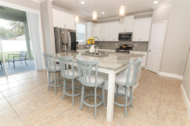 kitchen featuring stainless steel appliances, a center island with sink, white cabinets, and decorative light fixtures