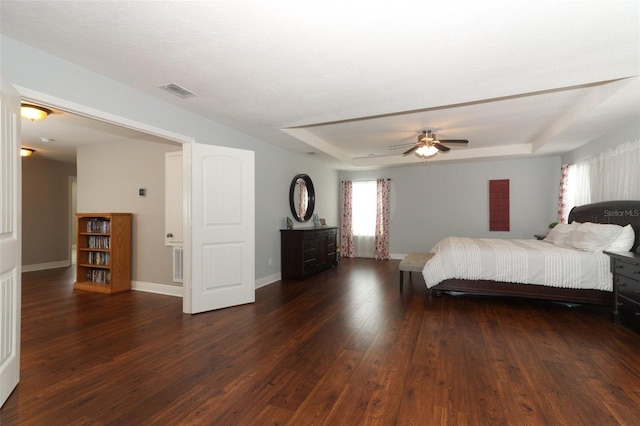 bedroom with dark wood-type flooring, ceiling fan, and a raised ceiling