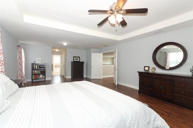 bedroom featuring dark wood-type flooring, ceiling fan, connected bathroom, and a tray ceiling