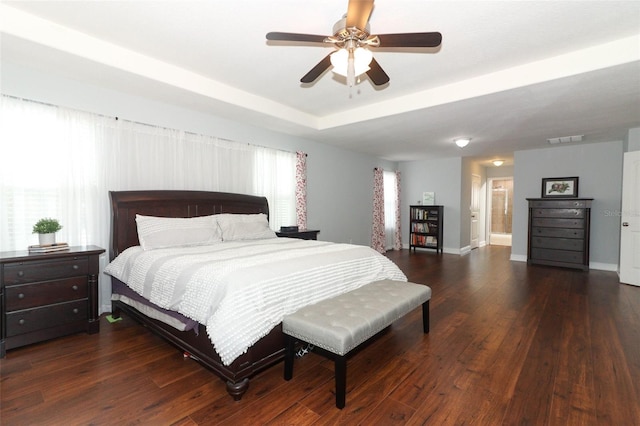 bedroom with ceiling fan, a tray ceiling, dark hardwood / wood-style floors, and connected bathroom