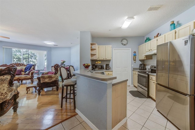 kitchen with appliances with stainless steel finishes, a kitchen breakfast bar, a textured ceiling, sink, and kitchen peninsula