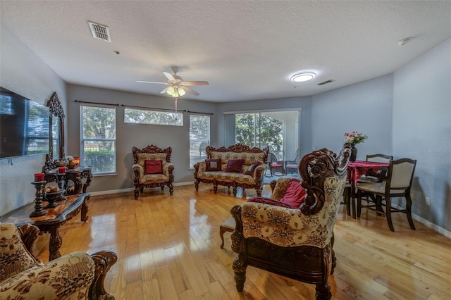 living room with a healthy amount of sunlight, light hardwood / wood-style flooring, ceiling fan, and a textured ceiling