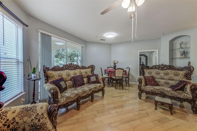 living room featuring light hardwood / wood-style floors, built in shelves, a textured ceiling, and ceiling fan