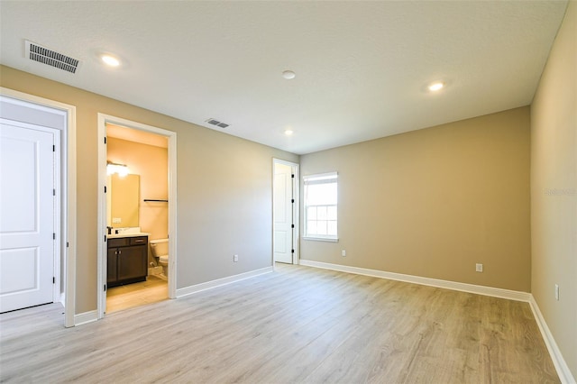 unfurnished bedroom with baseboards, visible vents, ensuite bath, and light wood finished floors