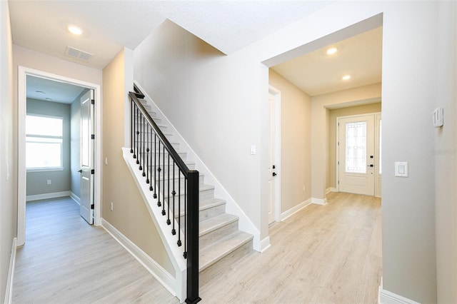 stairs with baseboards, wood finished floors, visible vents, and a healthy amount of sunlight