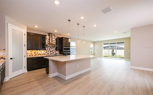 kitchen with wall chimney range hood, visible vents, light countertops, and backsplash