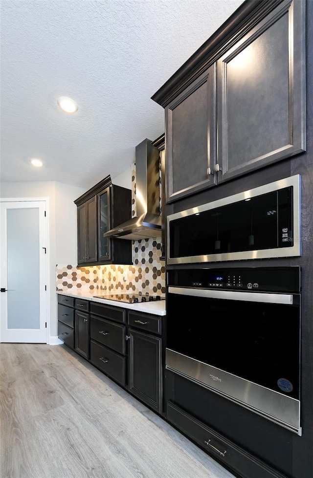 kitchen featuring light wood finished floors, wall chimney range hood, light countertops, a textured ceiling, and black appliances