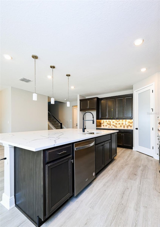 kitchen featuring a sink, light stone countertops, dishwasher, light wood finished floors, and an island with sink