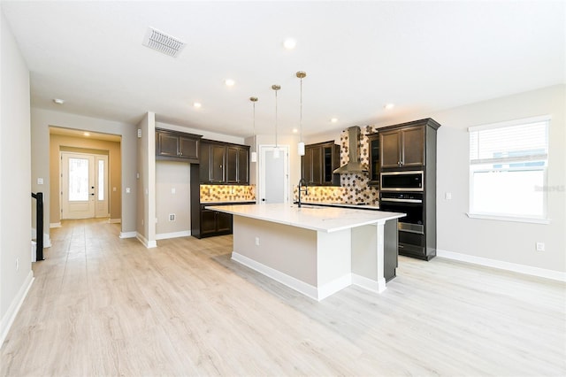 kitchen with wall oven, decorative backsplash, stainless steel microwave, wall chimney range hood, and a sink