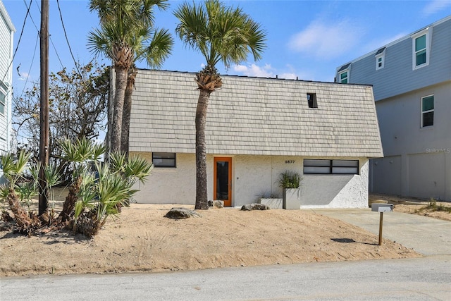 view of front of property featuring mansard roof, concrete driveway, and stucco siding