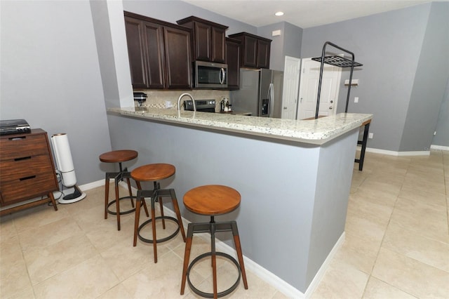 kitchen with a kitchen bar, dark brown cabinets, appliances with stainless steel finishes, kitchen peninsula, and backsplash