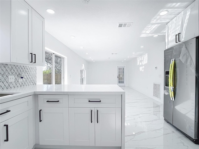 kitchen featuring white cabinets, kitchen peninsula, stainless steel fridge, and decorative backsplash