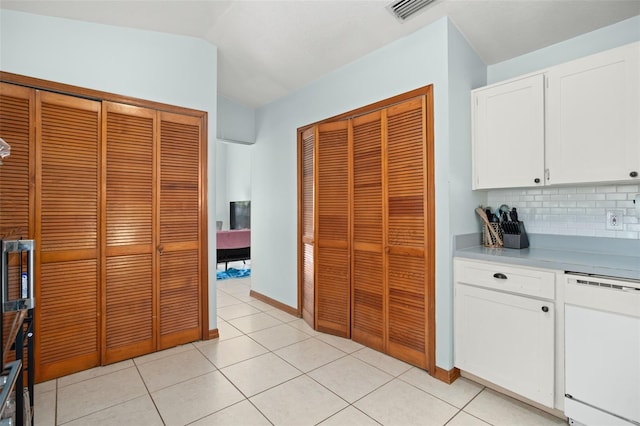 kitchen featuring light tile patterned flooring, vaulted ceiling, white dishwasher, white cabinets, and backsplash