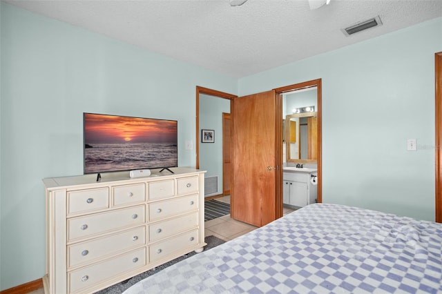 bedroom featuring sink, light tile patterned floors, a textured ceiling, and ensuite bathroom