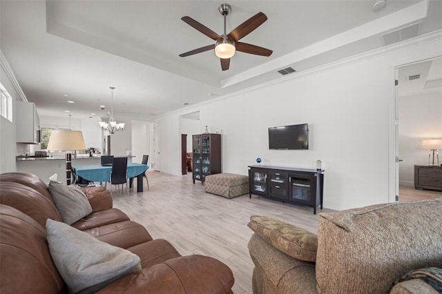 living room featuring ceiling fan with notable chandelier, ornamental molding, a tray ceiling, and light hardwood / wood-style floors