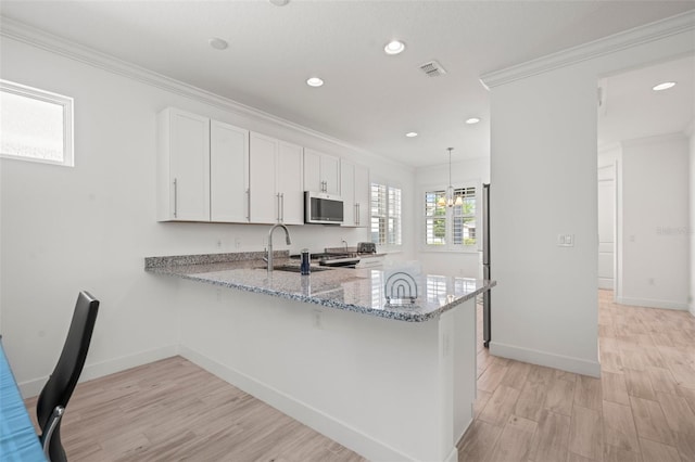 kitchen with white cabinetry, light stone countertops, crown molding, and kitchen peninsula