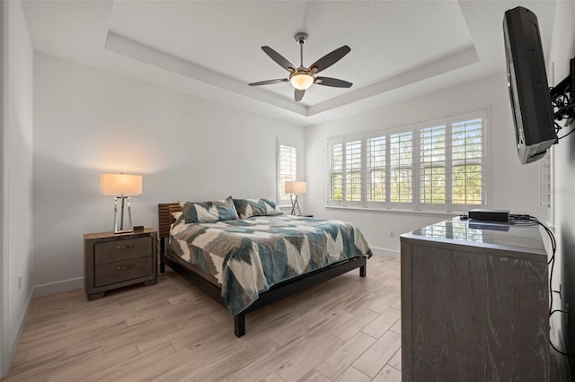 bedroom with light hardwood / wood-style flooring, ceiling fan, and a tray ceiling