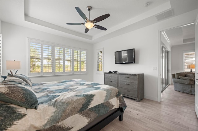 bedroom with ceiling fan, a tray ceiling, and light hardwood / wood-style flooring