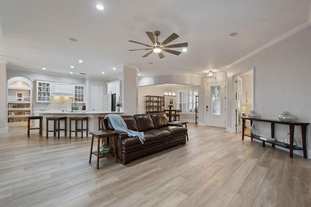 living room with sink, crown molding, ceiling fan with notable chandelier, and light hardwood / wood-style floors