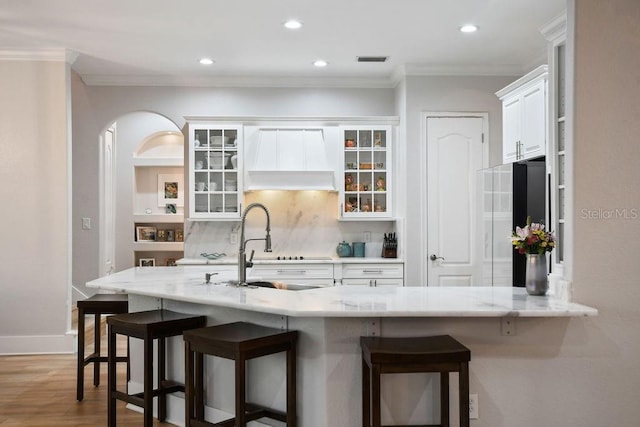 kitchen featuring premium range hood, crown molding, white cabinets, and a kitchen breakfast bar