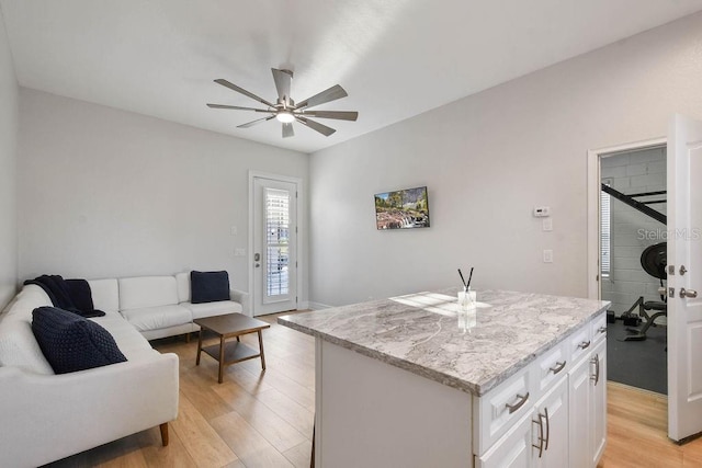 kitchen featuring a kitchen island, white cabinetry, light stone counters, ceiling fan, and light hardwood / wood-style floors