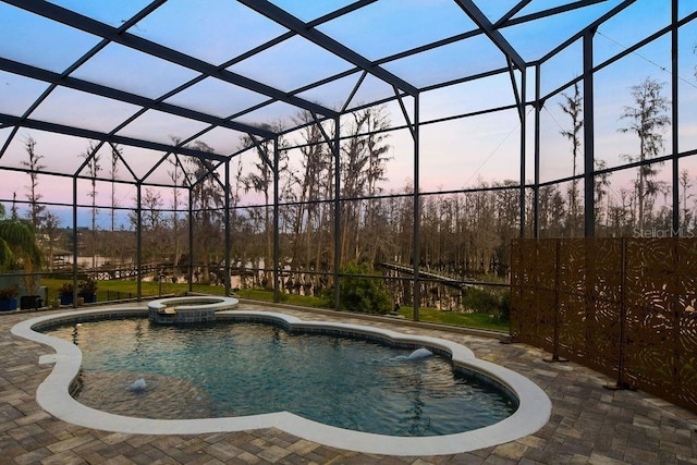 pool at dusk featuring a patio, a lanai, and an in ground hot tub