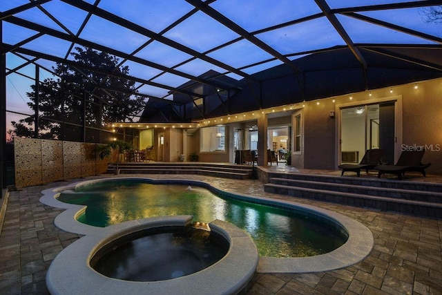 pool at dusk featuring an in ground hot tub, a patio area, and glass enclosure