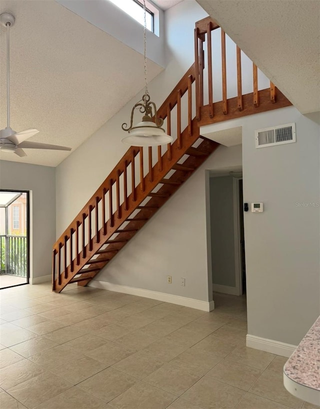 stairway featuring ceiling fan, tile patterned floors, a textured ceiling, and a towering ceiling