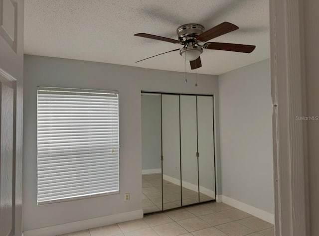 unfurnished bedroom with light tile patterned flooring, multiple windows, ceiling fan, a textured ceiling, and a closet