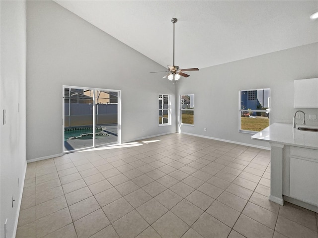 unfurnished living room featuring high vaulted ceiling, sink, light tile patterned floors, and ceiling fan