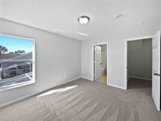 unfurnished bedroom with ensuite bathroom, carpet, and a textured ceiling