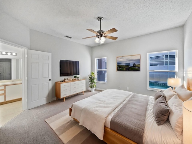 carpeted bedroom with ensuite bathroom, ceiling fan, and a textured ceiling